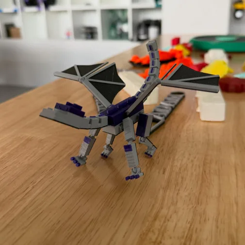 Pohyblivý drak vytištěný na 3D tiskárně, stojí na dřevěném stole