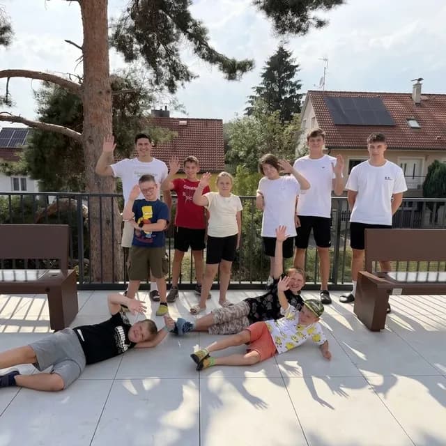 Děti s lektory na terase po letním táboře v Karlových Varech, mávají do objektivu